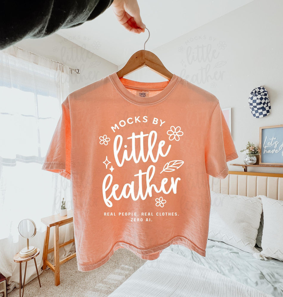 a peachy comfort colors 3023cl t-shirt with bold white text that says 'Mocks by Little Feather – Real People. Real Clothes. Zero AI.' surrounded by doodle-style flowers and feathers. Trendy Etsy-style mockup featuring real model photography for print-on-demand sellers.