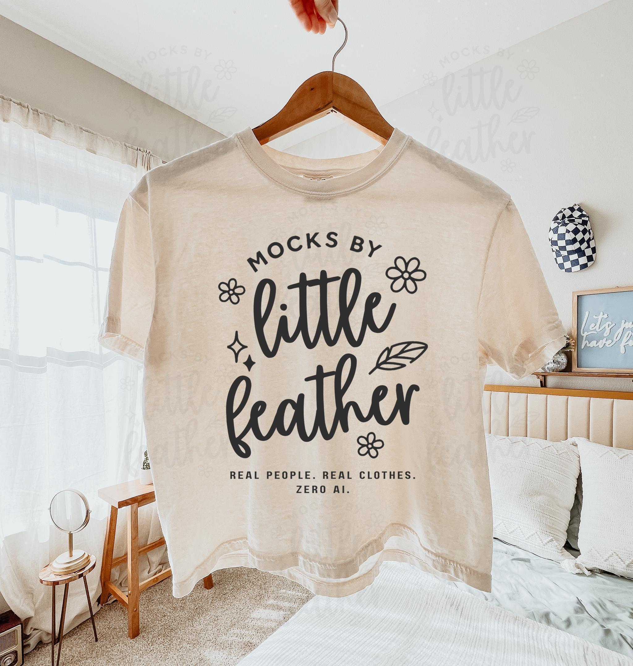 An ivory comfort colors 3023cl t-shirt with bold white text that says 'Mocks by Little Feather – Real People. Real Clothes. Zero AI.' surrounded by doodle-style flowers and feathers. Trendy Etsy-style mockup featuring real product photography for print-on-demand sellers.